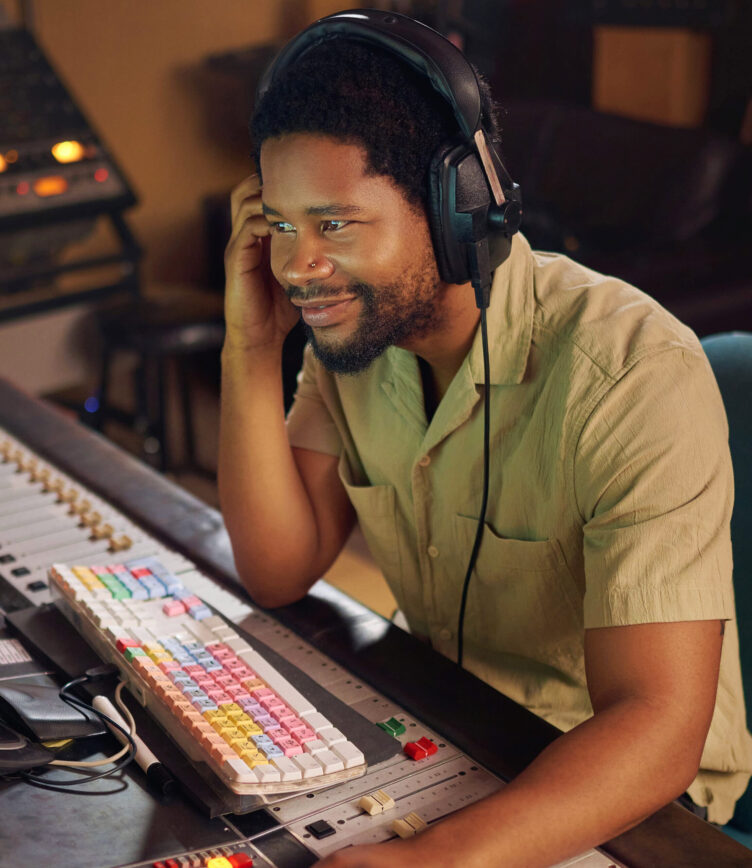 Ein Mann mit Kopfhörern sitzt in einem Tonstudio an einem Mischpult, bedient die Technik und hört konzentriert zu.