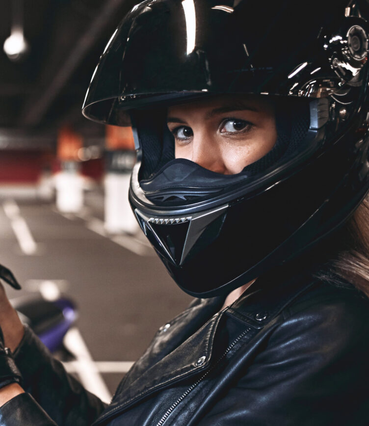 Eine Frau im schwarzen Motorradhelm und Lederjacke schaut direkt in die Kamera, bereit für eine Action-Szene.