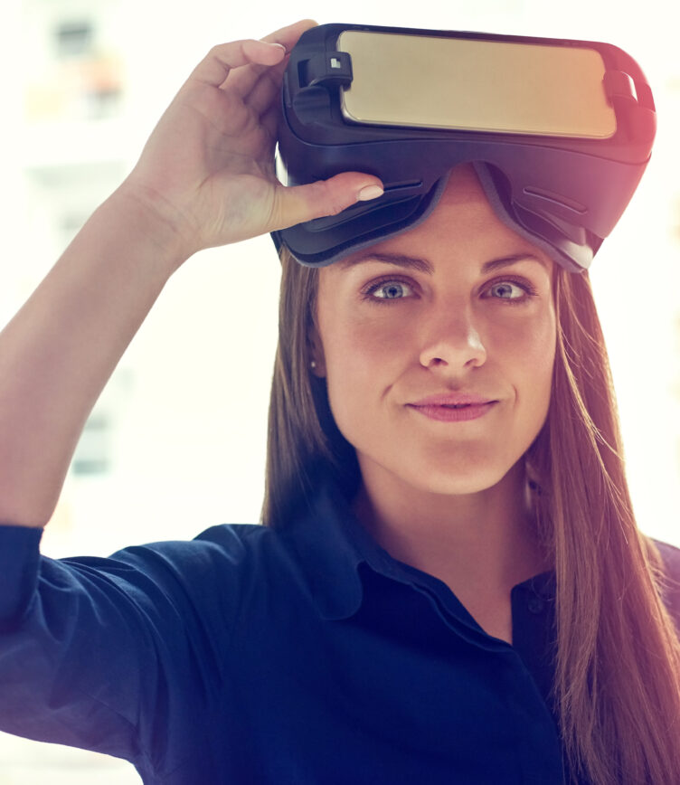 Eine Person trägt eine VR-Brille und hält sie mit beiden Händen. Sie trägt ein dunkelblaues Hemd und hat lange, braune Haare.