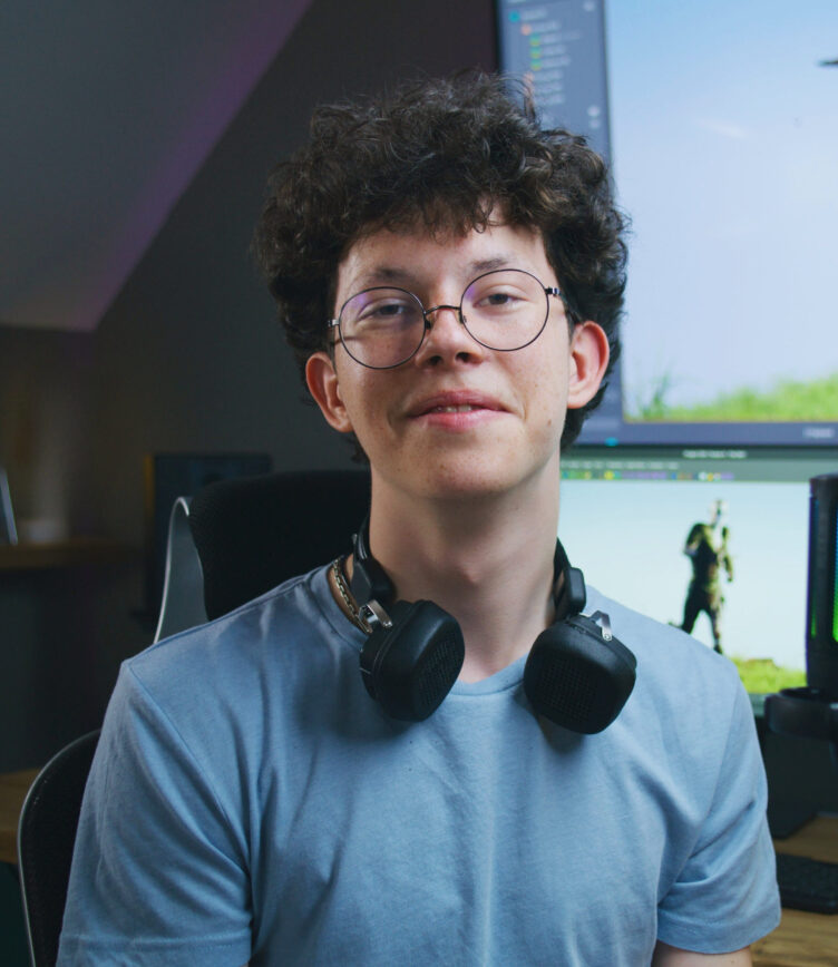 Junger Mann mit Brille und Kopfhörern sitzt in einem Gaming-Setup vor einem Bildschirm mit Videospiel.