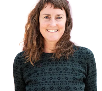 Frau mit schulterlangen, braunen, welligen Haaren, die lächelt und einen schwarzen Pullover mit Muster trägt. Hintergrund ist weiß.