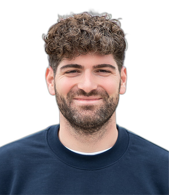 Freundlich lächelnder Mann mit kurzen, lockigen dunklen Haaren und Bart, der einen dunkelblauen Pullover mit Reißverschluss trägt.