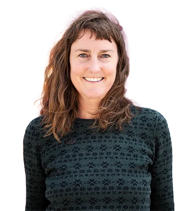 Frau mit schulterlangen, braunen, welligen Haaren, die lächelt und einen schwarzen Pullover mit Muster trägt. Hintergrund ist weiß.