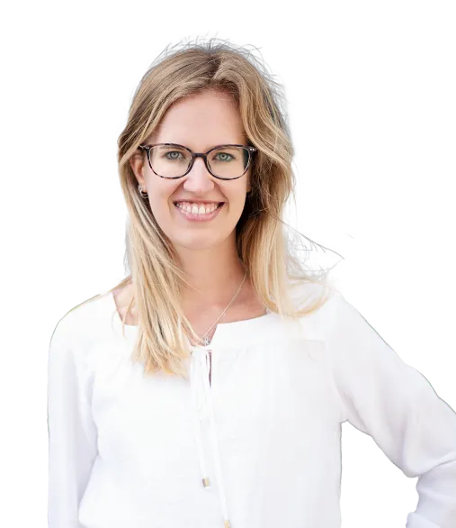 Junge Frau mit langen blonden Haaren und Brille, die lächelnd in die Kamera schaut. Sie trägt eine weiße Bluse und hat ihre rechte Hand in die Hüfte gestützt.