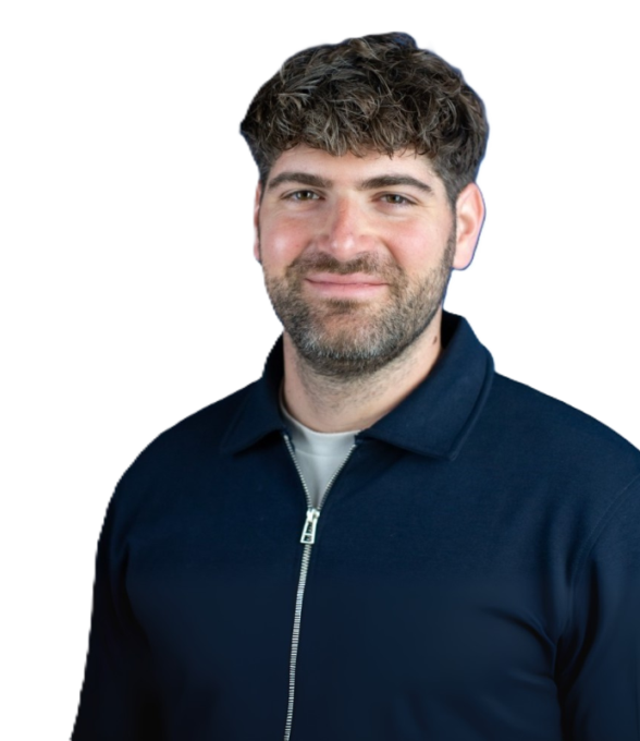 Freundlich lächelnder Mann mit kurzen, lockigen dunklen Haaren und Bart, der einen dunkelblauen Pullover mit Reißverschluss trägt.