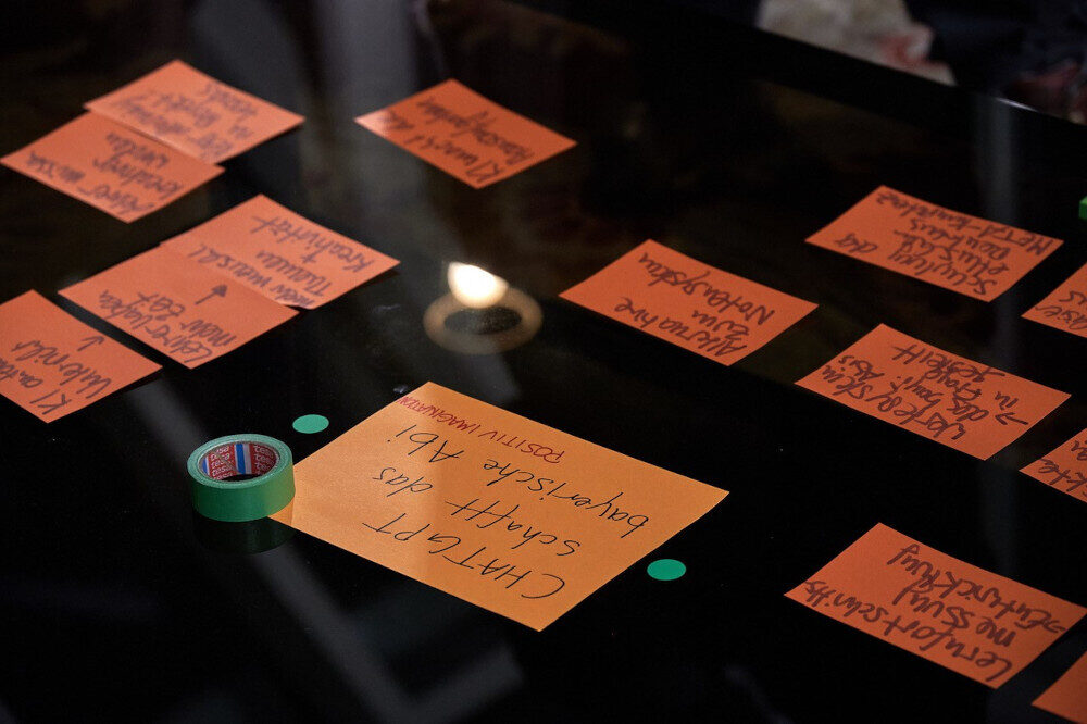 Orange Moderationskarten mit handgeschriebenen Notizen liegen auf einem schwarzen Tisch, daneben eine Rolle grünes Klebeband.