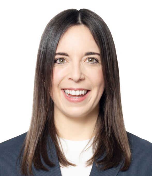 Das Portrait einer lachenden Frau mit schulterlangen, dunkelbraunen Haaren, die einen dunklen Blazer mit einem weißen Hemd trägt