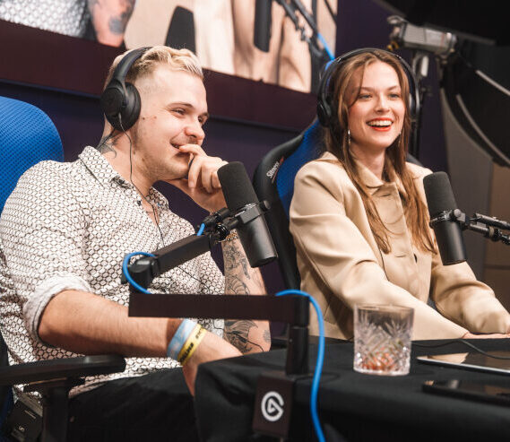 Zwei junge Menschen sitzen lachend mit Headsets und Mikrofonen in Gaming-Stühlen, während sie an einer Podcast- oder Streaming-Aufnahme teilnehmen.