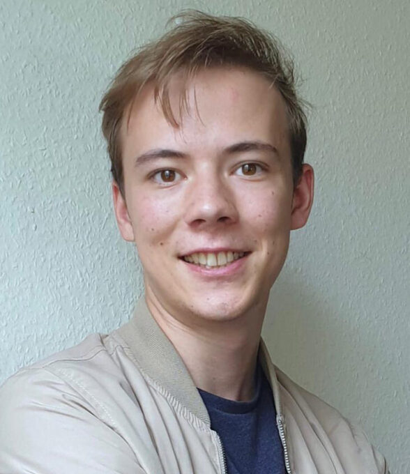 Felix Graf steht mit verschränkten Armen vor einer hellen Wand. Er trägt eine beige Bomberjacke über einem blauen T-Shirt.