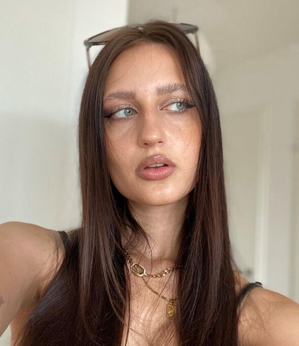 Matilda Jelitto posiert mit langen, glatten, braunen Haaren. Sie trägt eine schwarze Oberbekleidung und mehrere goldene Halsketten.