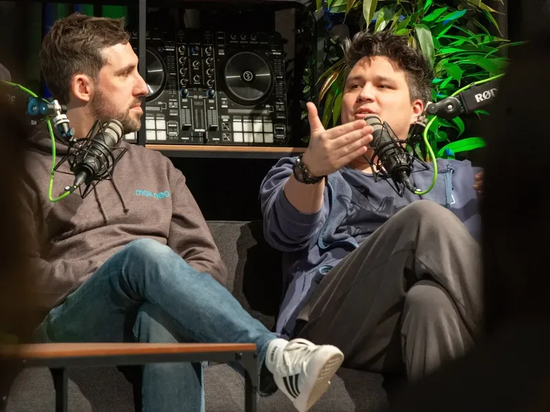 Musikproduzent Vincent Lee sitzt rechts, trägt einen grauen Hoodie und hat eine Hand erhoben. Links sitzt ein anderer Influencer in blauer Kleidung, beide sprechen in Mikrofone.