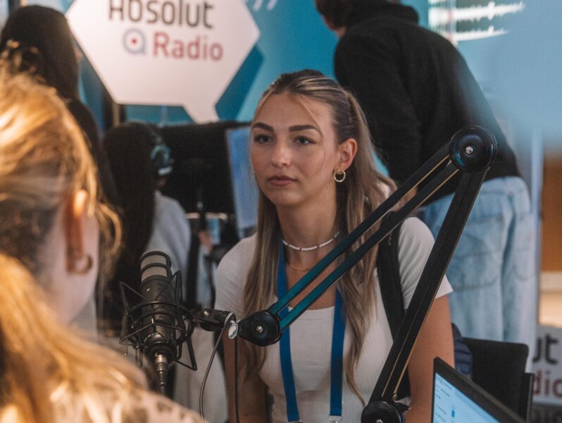 Junge Frau sitzt in einem Radiostudio und spricht in ein Mikrofon.