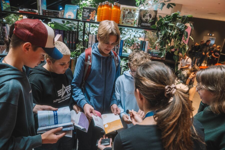 Eine Gruppe Jugendlicher steht um eine Frau, sie lesen gemeinsam in Broschüren und sprechen miteinander.